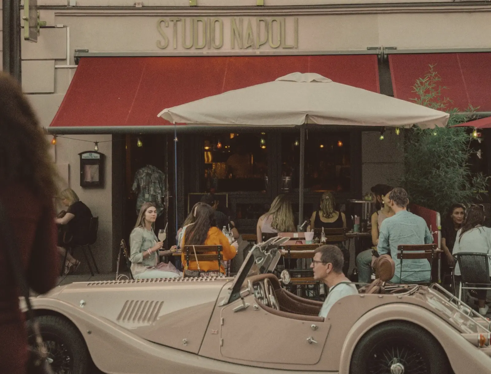 Studio Napoli — Maximilianstraße 67, Augsburg. Außenbereich mit Markise, Gäste, Vintage-Auto.